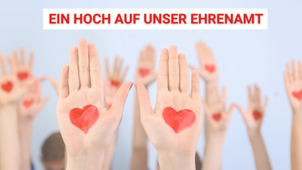 Ein Hoch auf unser Ehrenamt und mehrere Hände sind nach oben gestreckt mit Herzen auf den Innenflächen