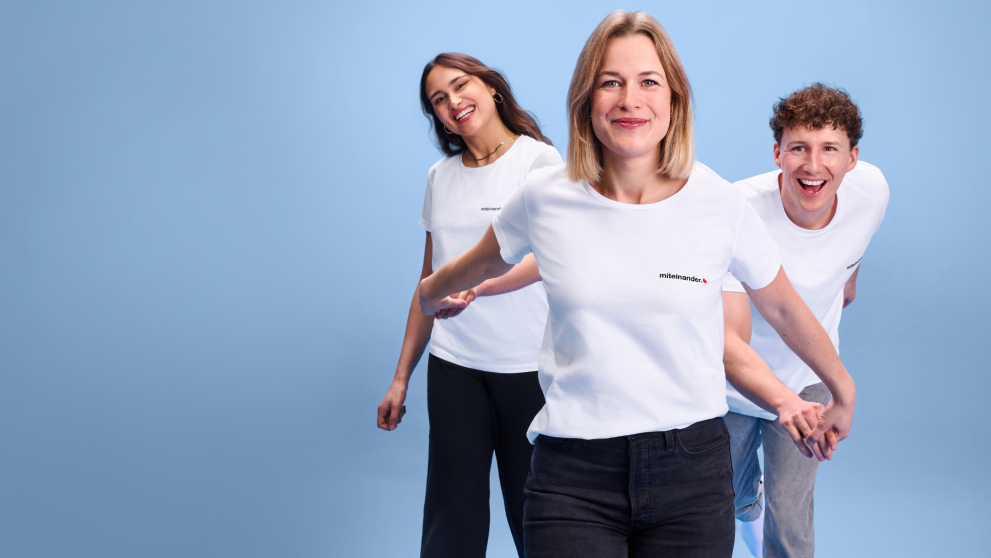 Drei Freunde, die sich an den Händen fassen. Alle mit dem miteinander-Shirt an. 