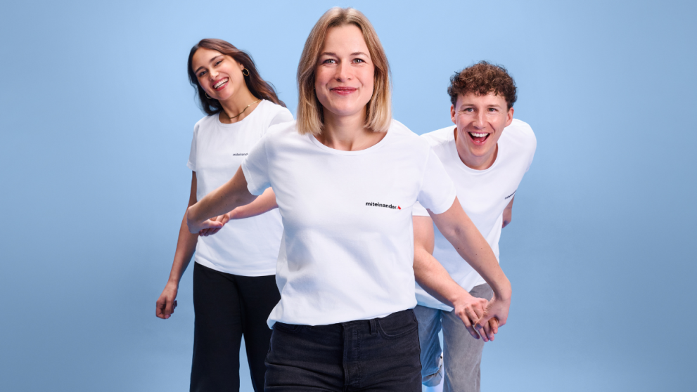 Drei Freunde, die sich an den Händen fassen. Alle mit dem miteinander-Shirt an. 