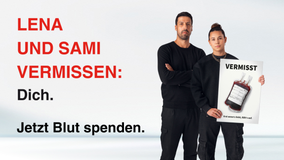 Lena und Sami halten ein Schild mit einer fehlenden Blutkonserve hoch. Auf dem Bild steht: Lena und Sami vermissen: Dich. Jetzt Blut spenden.