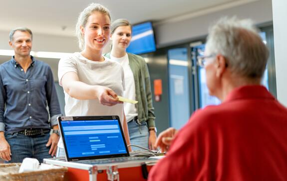 Junge Frau bei einem Blutspendetermin gibt ihren Blutspendeausweis zur Anmeldung ab