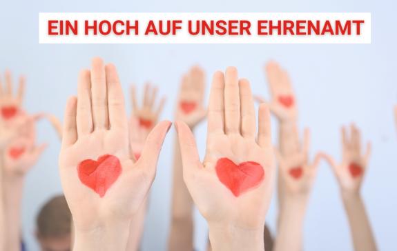 Ein Hoch auf unser Ehrenamt und mehrere Hände sind nach oben gestreckt mit Herzen auf den Innenflächen