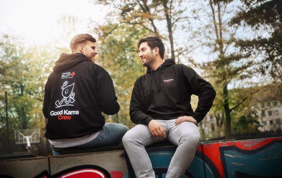 Zwei Männer mit Blutspende-Hoodie sitzen sich gegenüber