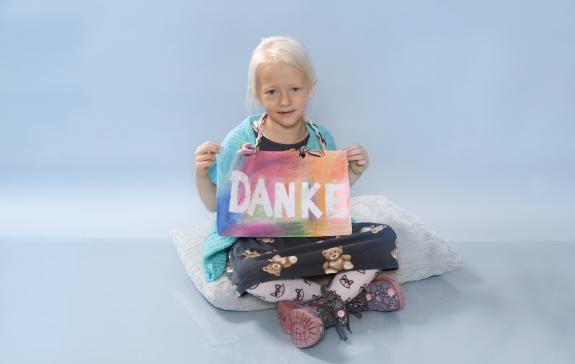 Eva sitzt im Schneidersitz auf dem Boden und hält ein "Danke"-Schild ins Bild