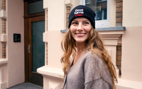 Eine freundlich lächelnde Frau trägt den schwarzen Good Karma Crew-Beanie