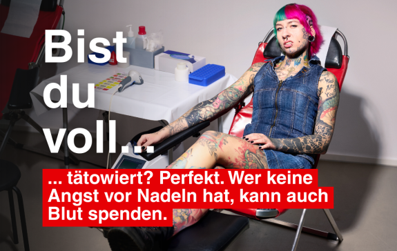 Eine voll tätowierte Frau auf einer Spendeliege. 