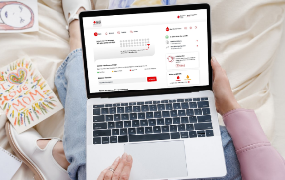 Eine Person sitzt auf dem Bett und schaut auf einen Laptop, bei dem der digitale spenderservice geöffnet ist.