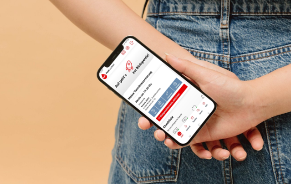Eine Person hällt ein Handy hinter dem Rücken, auf dem Bildschirm ist die App zu sehen